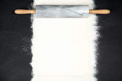 Photo of Flour and rolling pin on black table, flat lay