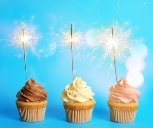 Birthday cupcakes with sparklers on light blue background