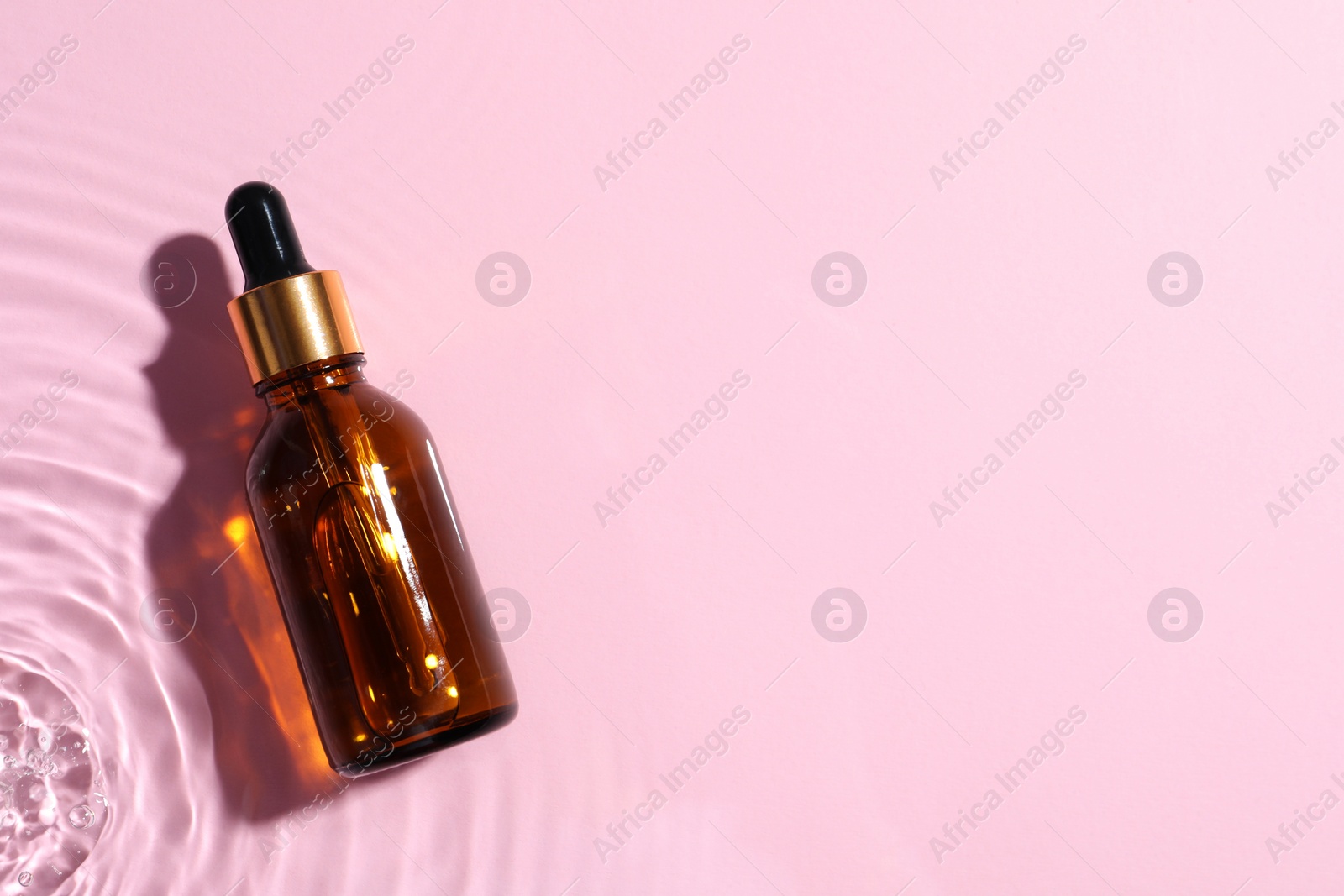 Photo of Bottle of cosmetic oil in water on pink background, top view. Space for text