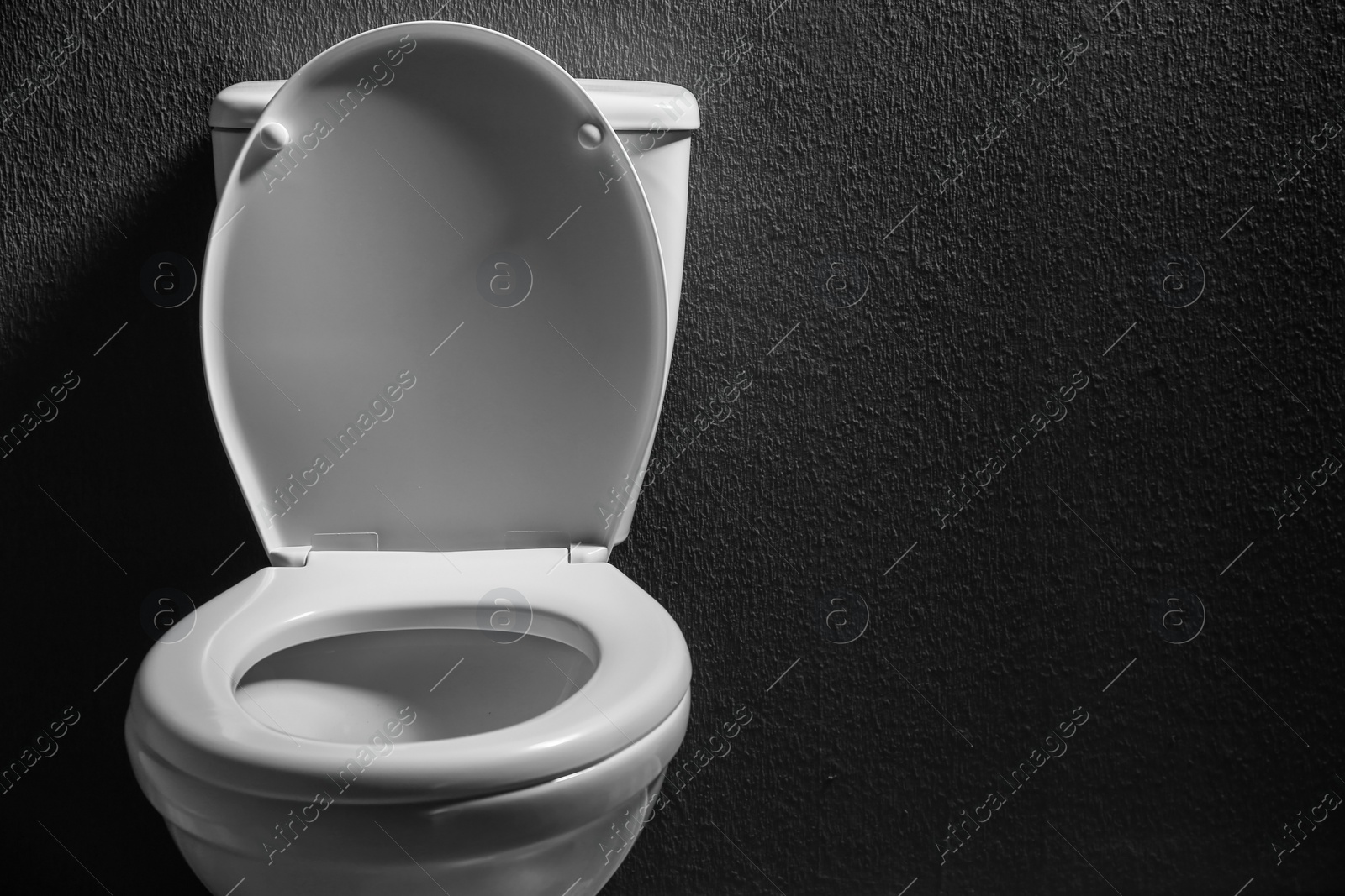 Photo of New ceramic toilet bowl on dark background