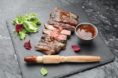 Photo of Pieces of delicious roasted beef meat with sauce and greens on black table