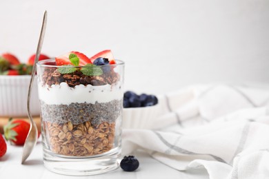 Photo of Tasty granola with berries, yogurt and chia seeds in glass on white table, space for text