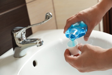 Photo of Man pouring mouthwash from bottle into cap in bathroom, closeup. Teeth care