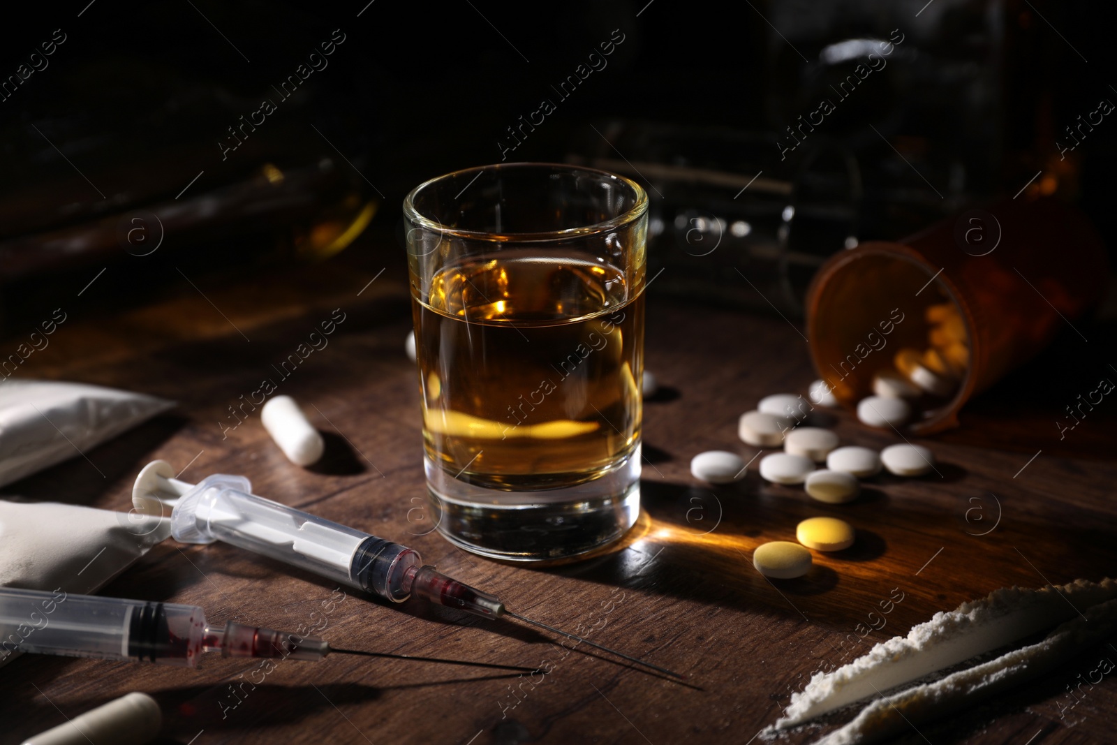 Photo of Alcohol and drug addiction. Whiskey in glass, syringes, pills and cocaine on wooden table