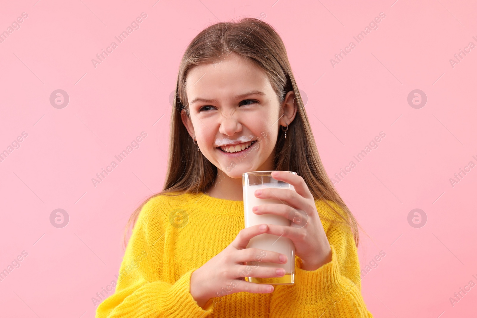 Photo of Happy little girl with milk mustache holding glass of tasty dairy drink on pink background