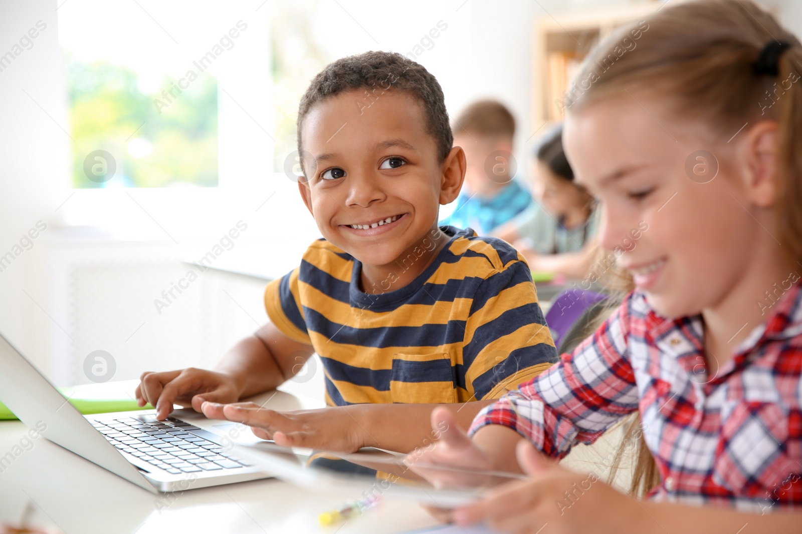 Photo of Cute little children with gadgets sitting at desk in classroom. Elementary school