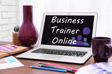 Modern laptop with text BUSINESS TRAINER ONLINE on wooden table indoors