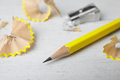 Photo of Pencil, sharpener and shavings on white wooden table, closeup