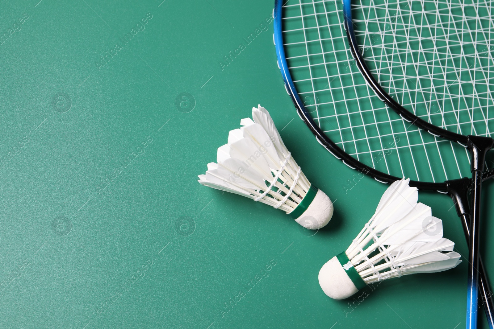Photo of Feather badminton shuttlecocks and rackets on green background, flat lay. Space for text