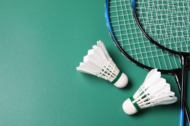 Photo of Feather badminton shuttlecocks and rackets on green background, flat lay. Space for text