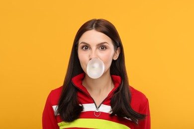 Photo of Beautiful woman blowing bubble gum on orange background