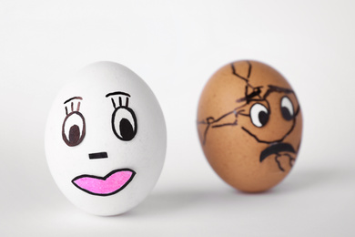 Photo of Eggs with drawn faces on white background, closeup. Concept of jealousy
