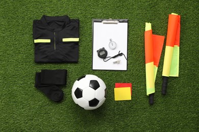 Photo of Uniform, soccer ball and other referee equipment on green grass, flat lay