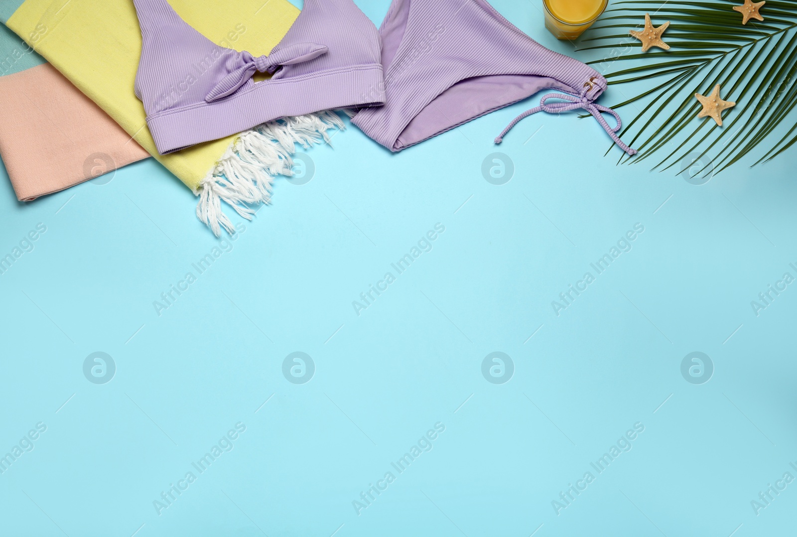 Photo of Beach towel, swimsuit and palm leaf on light blue background, flat lay. Space for text