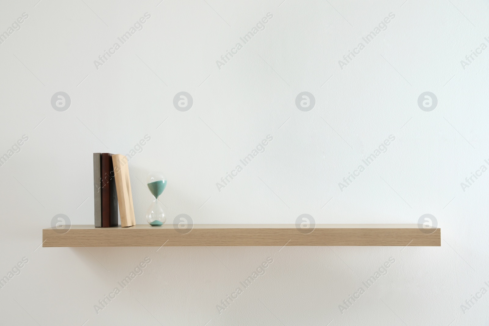 Photo of Wooden shelf with sand clock and books on light wall