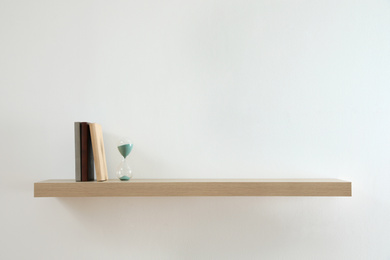 Photo of Wooden shelf with sand clock and books on light wall