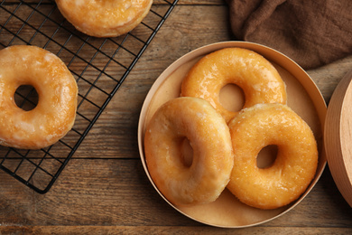 Photo of Delicious donuts in box on wooden table, flat lay