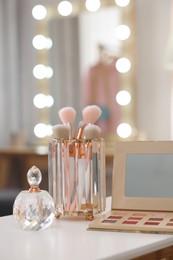 Photo of Set of brushes, eyeshadow palette and perfume on white table in makeup room