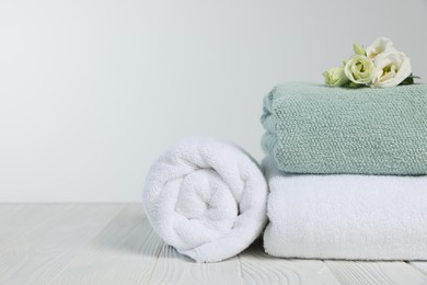 Photo of Soft towels with flowers on wooden table against white background, space for text