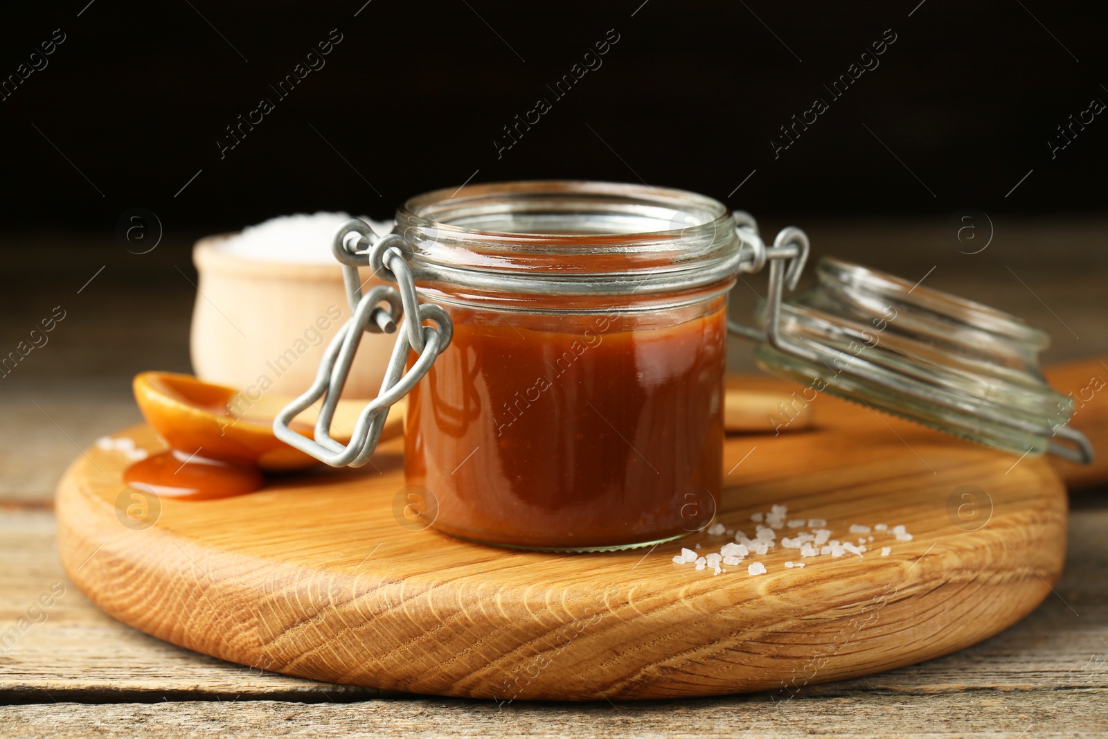 Photo of Tasty salted caramel in jar and salt on table, closeup