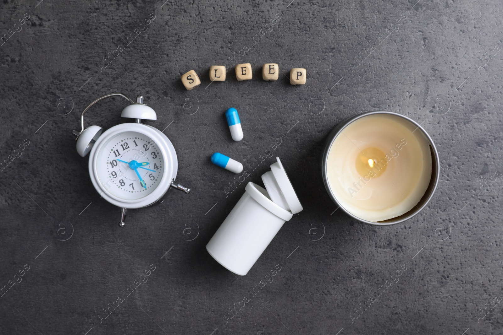 Photo of Word Sleep made of wooden cubes near alarm clock, candle and pills on grey background, flat lay. Insomnia treatment