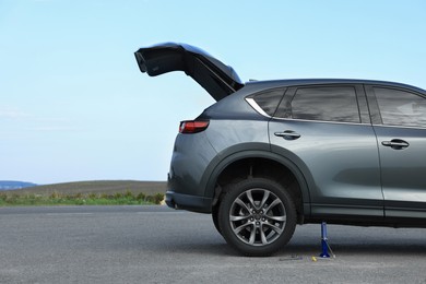 Photo of Car lifted by scissor jack on roadside outdoors. Tire puncture