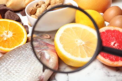 Photo of Different products with magnifier focused on fish and lemon, closeup. Food allergy concept