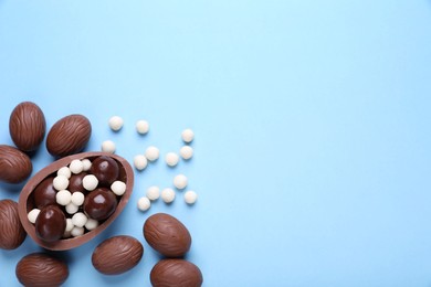 Photo of Delicious chocolate eggs and candies on light blue background, flat lay. Space for text