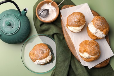 Photo of Delicious profiteroles filled with cream and teapot on green background, flat lay