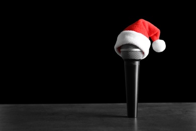 Photo of Microphone with Santa hat on table against black background. Christmas music concept