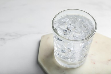 Photo of Glass of soda water with ice on white marble table, closeup. Space for text