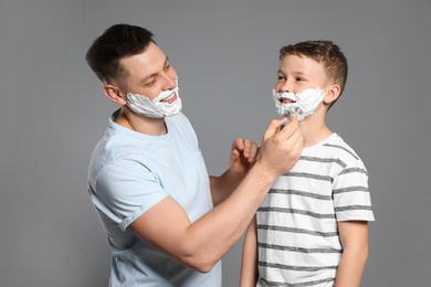 Photo of Dad applying shaving foam on son's face, grey background