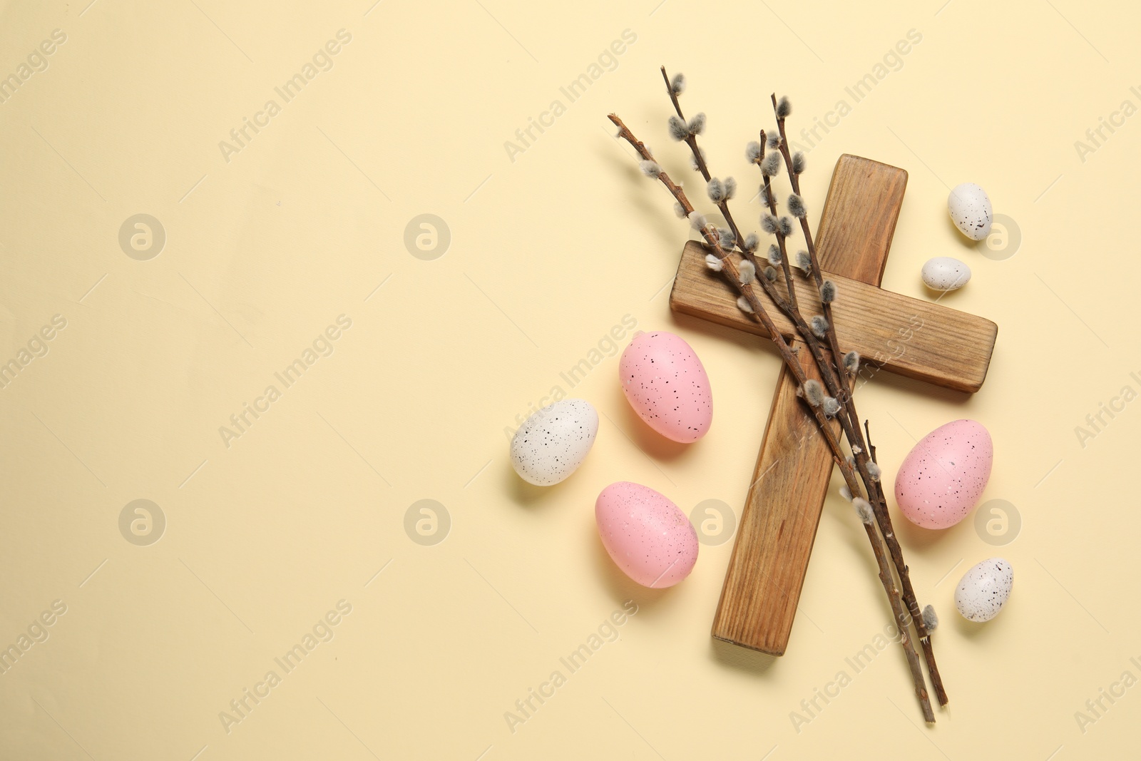 Photo of Wooden cross, painted Easter eggs and willow branches on beige background, flat lay. Space for text