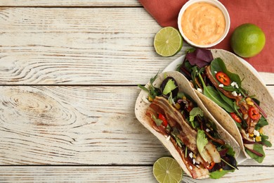 Photo of Delicious tacos with fried bacon, lime and sauce on white wooden table, flat lay. Space for text
