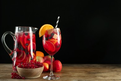 Photo of Glass and jug of Red Sangria with fruits on wooden table against black background. Space for text