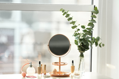 Photo of Mirror and makeup products on table near window indoors