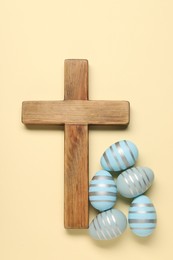 Photo of Wooden cross and painted Easter eggs on beige background, flat lay