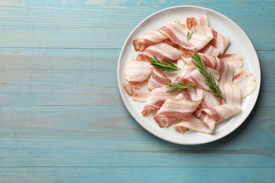 Photo of Slices of raw bacon and rosemary on light blue wooden table, top view. Space for text