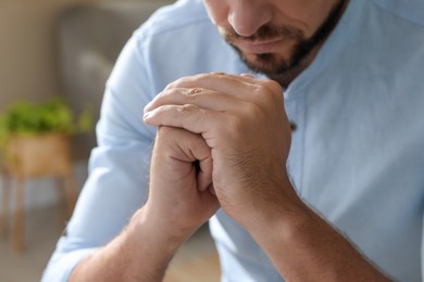 Photo of Religious man with clasped hands praying indoors, closeup