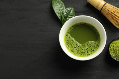 Photo of Cup of fresh matcha tea, green powder and bamboo whisk on black wooden table, flat lay. Space for text
