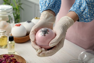 Photo of Woman in gloves making bath bomb at white table , closeup