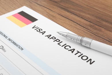 Photo of Immigration to Germany. Visa application form and pen on wooden table, closeup