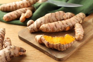 Many raw turmeric roots on wooden table, closeup