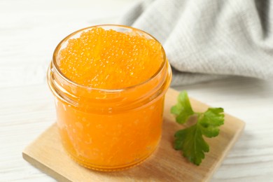 Photo of Fresh pike caviar in glass jar and parsley on white wooden table, closeup