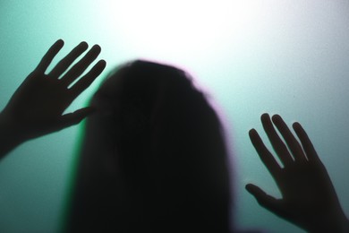 Photo of Silhouette of creepy ghost behind glass against color background