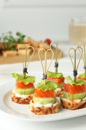 Photo of Tasty canapes with salmon, cucumber, bread and cream cheese on white table, closeup