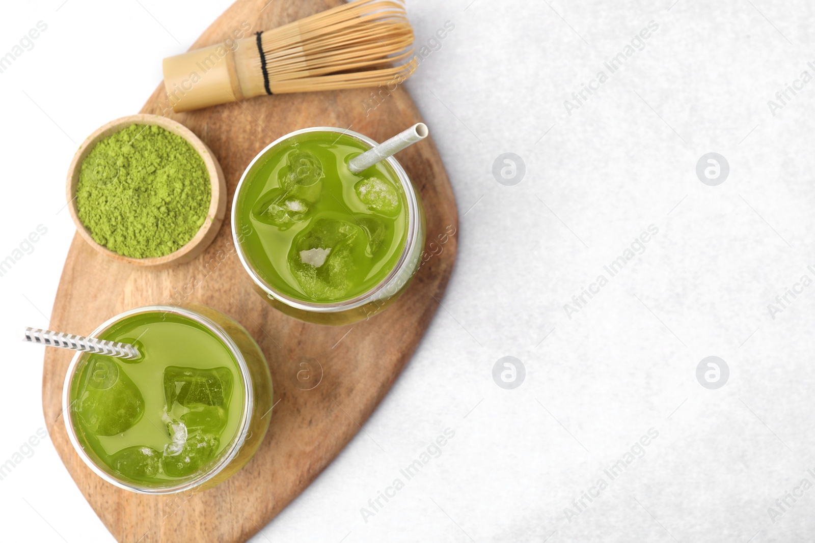 Photo of Delicious iced green matcha tea, powder and bamboo whisk on white table, top view. Space for text