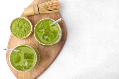 Photo of Delicious iced green matcha tea, powder and bamboo whisk on white table, top view. Space for text