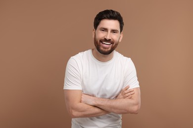 Photo of Handsome man with crossed arms laughing on light brown background