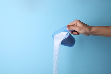 Photo of Woman pouring laundry detergent from measuring container against blue background, closeup. Space for text